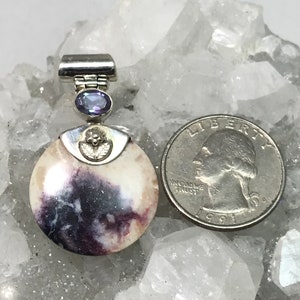 May include: A round, white and purple stone pendant with a silver bail and a small amethyst gemstone. The pendant is about the size of a quarter.