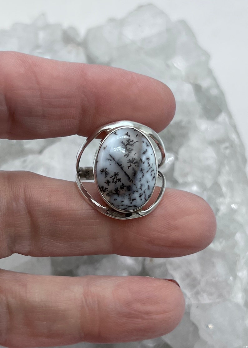 May include: A silver ring with an oval-shaped dendritic agate stone. The stone is white with black dendritic patterns.