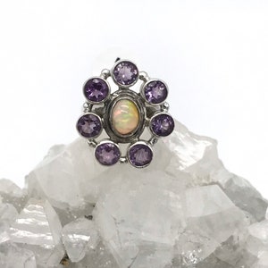 May include: A silver ring with a white opal gemstone surrounded by eight amethyst gemstones.
