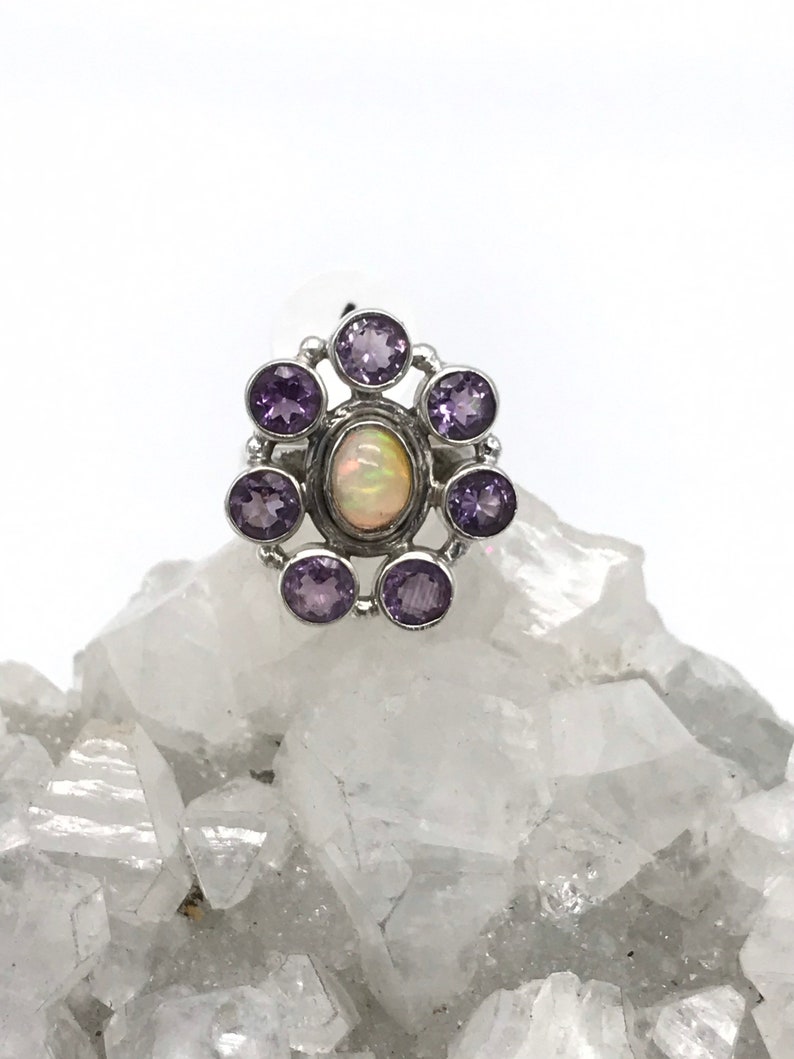 May include: A silver ring with a white opal gemstone surrounded by eight amethyst gemstones.