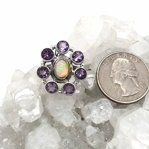 May include: A silver ring with a white opal gemstone surrounded by eight purple amethyst gemstones.