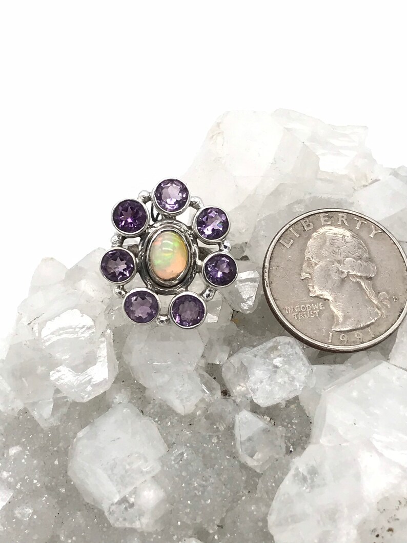 May include: A silver ring with a white opal gemstone surrounded by eight purple amethyst gemstones.
