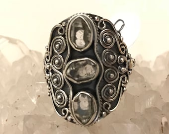 Könnte beinhalten: Ein silberner Ring mit drei klaren Quarzsteinen, die in einem filigranen Design eingefasst sind.