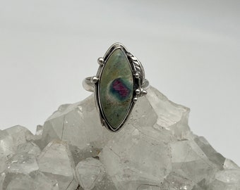 May include: A silver ring with a green and pink gemstone set in a marquise shape.