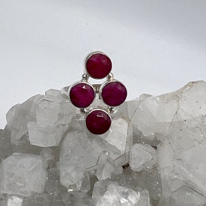 May include: A silver ring with four round, deep pink gemstones set in a cluster design.