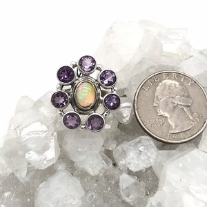 May include: A silver ring with a white opal gemstone surrounded by eight purple amethyst stones.