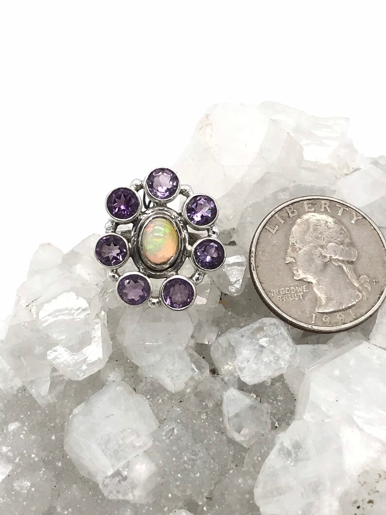 May include: A silver ring with a white opal gemstone surrounded by eight purple amethyst stones.