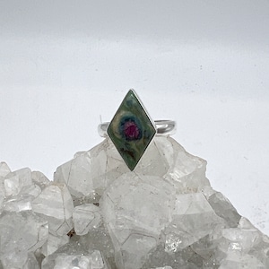 May include: A silver ring with a green and pink gemstone set in a diamond-shaped setting.