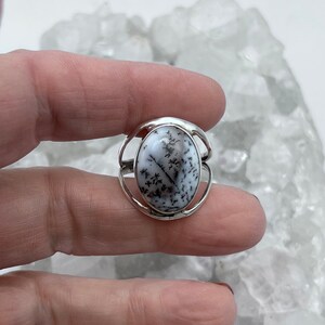 May include: A silver ring with a white dendritic agate oval stone. The stone has a natural pattern of black dendrites.