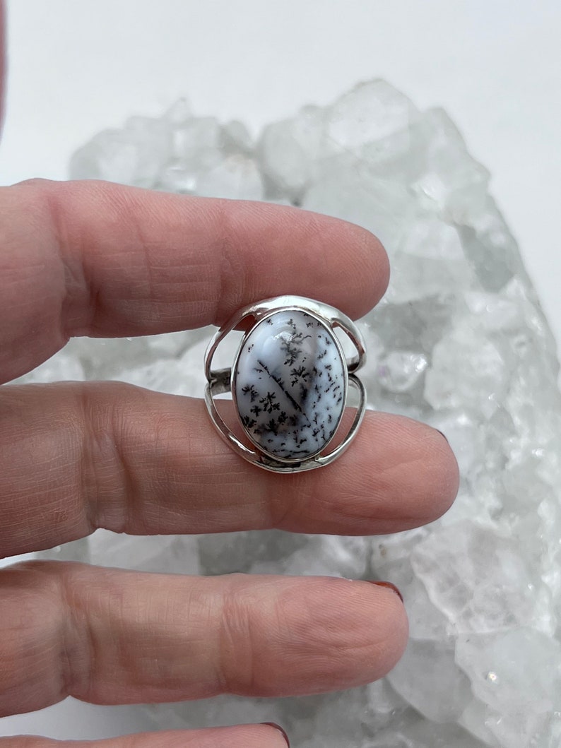 May include: A silver ring with a white dendritic agate oval stone. The stone has a natural pattern of black dendrites.
