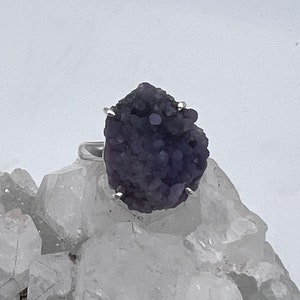 May include: A purple amethyst ring featuring a unique, rough-cut stone set in a silver band.