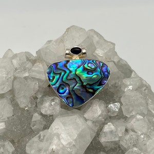 May include: A silver pendant featuring a heart-shaped abalone shell with iridescent blue, green, and purple hues. A small black gemstone is set in the bail.