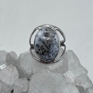May include: A silver ring with a white and black dendritic agate stone set in a bezel setting.