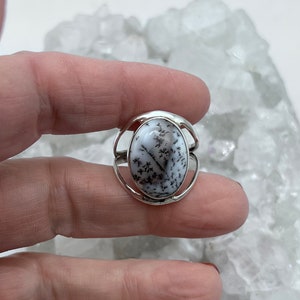 May include: A silver ring with a white and black dendritic agate stone. The stone is oval shaped and set in a silver band.