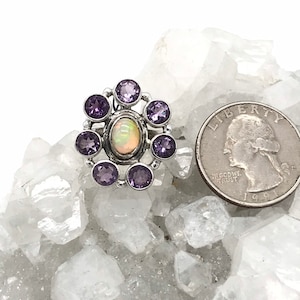 May include: A silver ring with a white opal gemstone surrounded by eight purple amethyst stones.