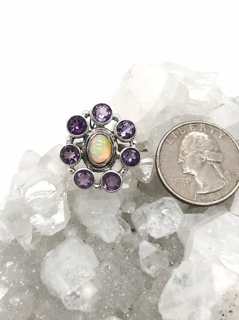 May include: A silver ring with a white opal gemstone surrounded by eight purple amethyst stones.