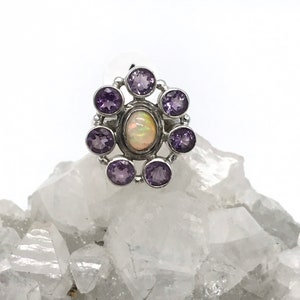 May include: A silver ring with a white opal gemstone surrounded by eight smaller amethyst gemstones.