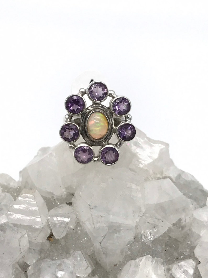 May include: A silver ring with a white opal gemstone surrounded by eight smaller amethyst gemstones.