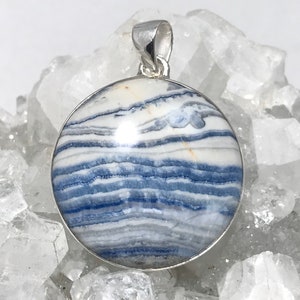 May include: A silver pendant featuring a round, blue and white banded agate stone. The stone has a polished, smooth surface and is set in a silver bezel.