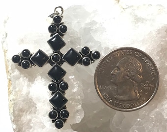 Puede incluir: Un colgante de plata en forma de cruz con piedras de ónix negro. La cruz es aproximadamente del tamaño de una moneda de 25 centavos de dólar estadounidense.