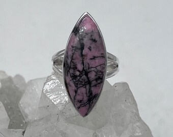 May include: A silver ring with a pink and black marbled stone set in a marquise shape.