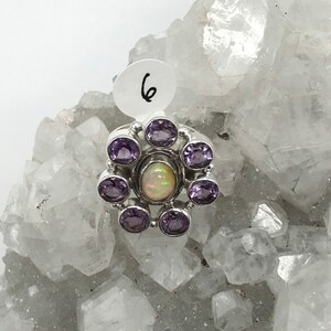 May include: A silver ring with a white opal gemstone surrounded by six amethyst gemstones.