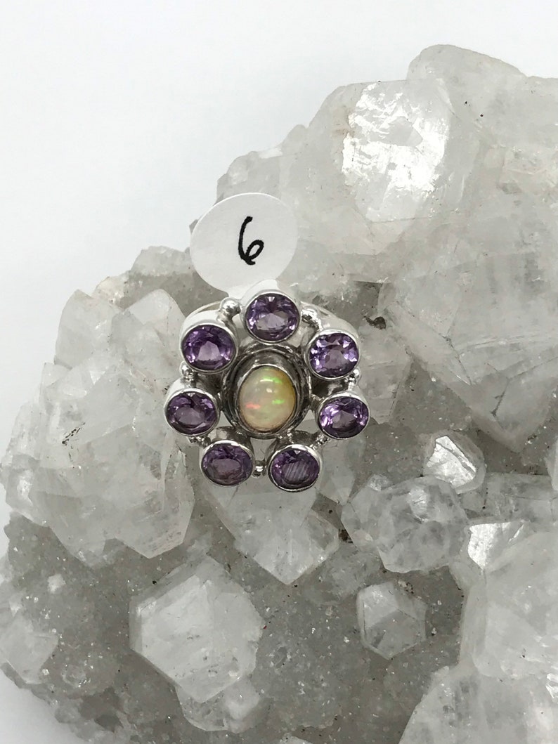 May include: A silver ring with a white opal gemstone surrounded by six amethyst gemstones.