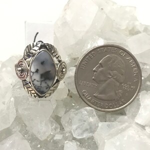 Pu&ograve; includere: Un anello d'argento con una pietra di agata bianca e nera incastonata in un design a spirale d'argento. L'anello &egrave; mostrato accanto a una moneta da 25 centesimi di dollaro americano per il confronto delle dimensioni.