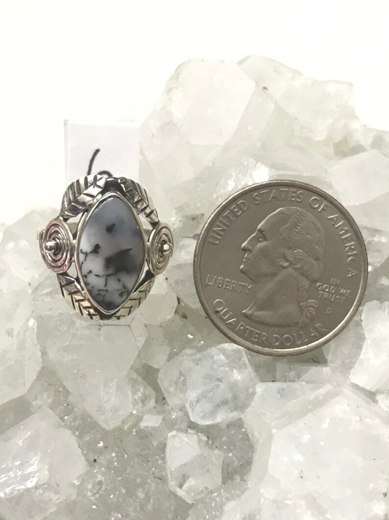 Pu&ograve; includere: Un anello d'argento con una pietra di agata bianca e nera incastonata in un design a spirale d'argento. L'anello &egrave; mostrato accanto a una moneta da 25 centesimi di dollaro americano per il confronto delle dimensioni.