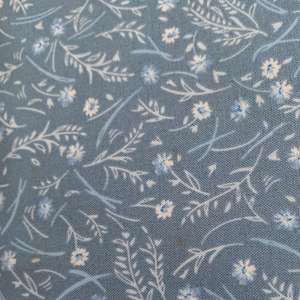 May include: A blue fabric with a white floral pattern. The fabric has a small-scale, repeating pattern of white flowers and blue stems.