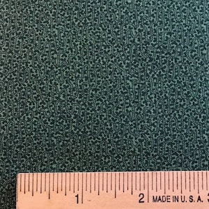 May include: A close-up of a dark green fabric with a subtle pattern of small, white dots. A wooden ruler with the text "MADE IN U.S.A." is placed on top of the fabric.