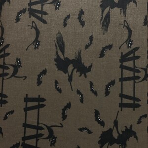 May include: A brown fabric with a repeating pattern of black silhouettes of witches flying on broomsticks, cats climbing fences, and bats. The fabric has a subtle texture.
