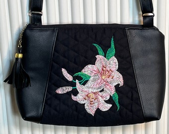 Ladies black faux leather purse/quilted embroidered flower on center of front, exterior zipper pocket on back, interior zip and slip pockets