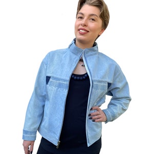 May include: A light blue denim jacket with a zip fastening and a decorative stitch detail on the front and sleeves.