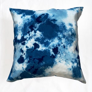Puede incluir: Una funda de coj&iacute;n de color azul y blanco con estampado tie-dye y forma cuadrada. La funda de coj&iacute;n tiene un patr&oacute;n suave y abstracto.