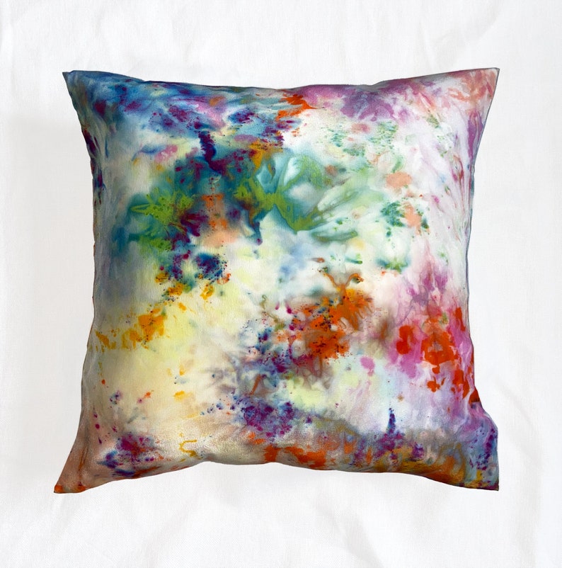 Puede incluir: Una funda de coj&iacute;n de tie-dye colorida con fondo blanco y salpicaduras de naranja, rosa, morado, azul y verde.