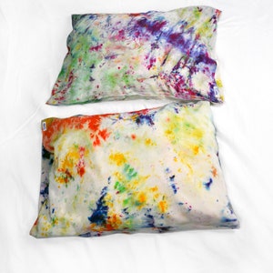 Puede incluir: Dos fundas de almohada de te&ntilde;ido anudado con fondo blanco y patrones de salpicaduras de colores. La funda de almohada de arriba tiene un patr&oacute;n de salpicaduras de morado, rosa, verde y azul. La funda de almohada de abajo tiene un patr&oacute;n de salpicaduras de rojo, naranja, amarillo, verde y azul.