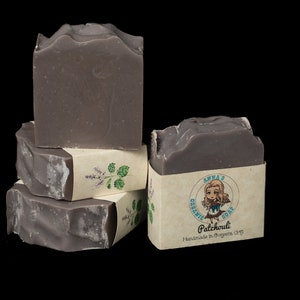 May include: Four bars of handmade, organic, purple-grey soap stacked on top of each other. The top bar has a label that reads "Anna's Organic Soap Patchouli Handmade in Oregon USA".