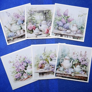 May include: A set of six square art prints. Each print features a watercolour illustration of teacups, teapots, and floral arrangements. The prints have a vintage aesthetic with soft colours and a garden theme. Each print has a white border.