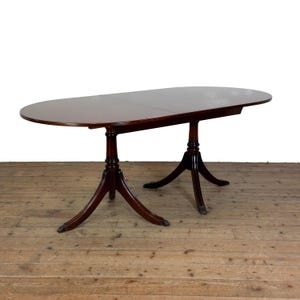 May include: An oval-shaped dark wood dining table with a smooth, polished surface. The table features two central pedestal bases, each with three curved legs that extend outward, providing structural support for the elongated tabletop.