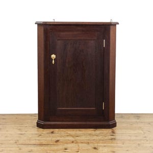 May include: A dark wood corner cabinet with a single door and a brass knob. The cabinet has a simple design with a slightly rounded top and bottom.