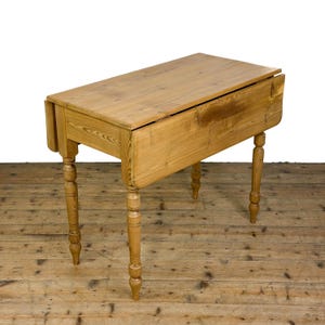 May include: A light brown wooden drop-leaf table featuring a rectangular top with two hinged side panels that can be folded down. The table is supported by four turned legs with a smooth finish, showcasing the natural grain and texture of the wood.