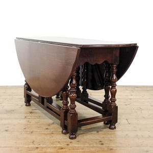 May include: A dark brown, antique drop-leaf table. The table features a rounded top with two drop leaves, supported by turned legs and a stretcher base. The wooden table has a warm, inviting appearance, and is approximately 120 cm long.