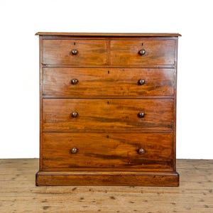 May include: A wooden chest of drawers with a warm brown finish. The piece features two small top drawers and three full-width drawers below. Each drawer is equipped with two round wooden knobs and a central keyhole, showcasing a natural wood grain.