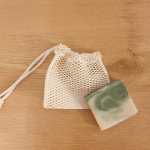 May include: A white mesh bag with a drawstring closure, containing a green and white bar of soap.