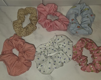 May include: A collection of six fabric hair scrunchies in various patterns and colors. The set includes a tan polka dot, a solid pink, a light blue floral, a dusty rose polka dot, a white with small blue flowers, and a pink with white lily print.