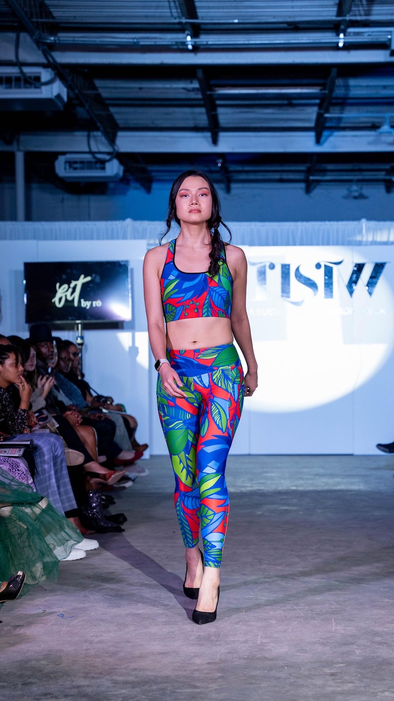 May include: A woman is modelling a blue, red and green patterned sports bra and leggings. The bra and leggings have a tropical leaf design. The woman is wearing black high heels and has her hair pulled back in a braid.