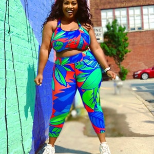 May include: A woman wearing a blue, green and red tropical print sports bra and leggings. The outfit has a cropped top and a high-waisted bottom.