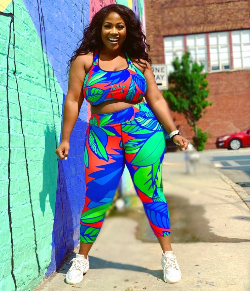 May include: A woman wearing a blue, green and red tropical print sports bra and leggings. The outfit has a cropped top and a high-waisted bottom.