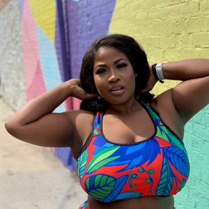 May include: A woman wearing a blue and red sports bra with a tropical leaf print. The bra has black straps and a black band around the bottom.